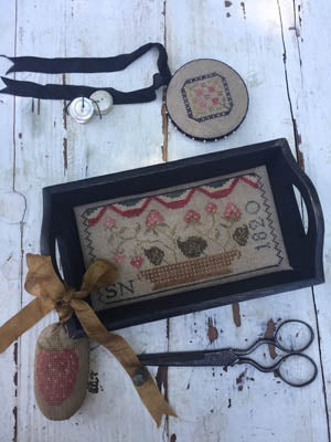 Handmade needlework tray with floral design, brown ribbon, scissors, and accessories on rustic table.