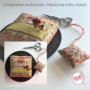 Embroidered autumn-themed cushion with scissors, featuring a house design in warm colors.