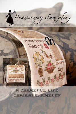Cross-stitch 'Thankful Life' charm pinkeep with floral designs in soft colors on a textured fabric background.