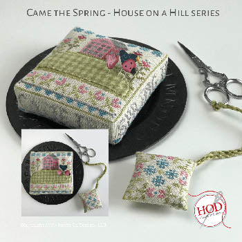 Came the Spring decorative cushion, green, stitched fabric, featuring a house design and flowers.