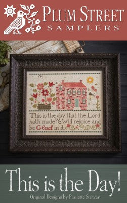Framed cross-stitch artwork titled 'This is the Day!' featuring a house, flowers, and inspirational text.