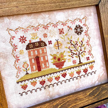 Embroidered cross-stitch artwork featuring a house, tree, and floral designs in warm colors.