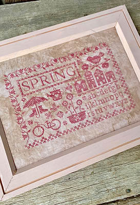 Framed spring-themed cross-stitch art in pink and beige featuring flowers, bicycles, and text.