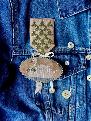 Handcrafted embroidered brooch featuring a swan on beige fabric, accented with green stitching and ribbon.