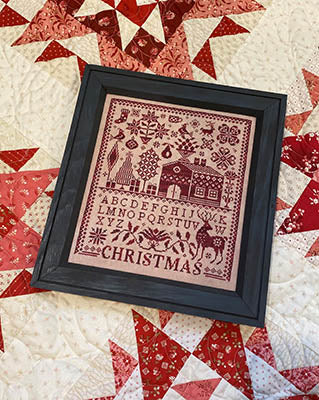 Framed vintage Christmas cross-stitch art, burgundy on beige, featuring letters and festive motifs.