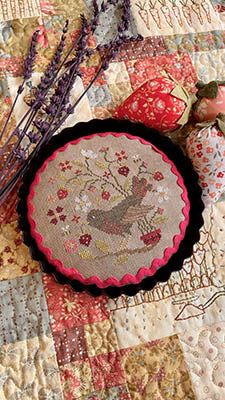 Embroidered round wall decor featuring a colorful bird and flowers, set against a quilted background.