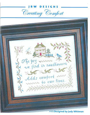 Framed cross-stitch design by Judy Whitman featuring a house, bird, and the phrase about needlework comfort.