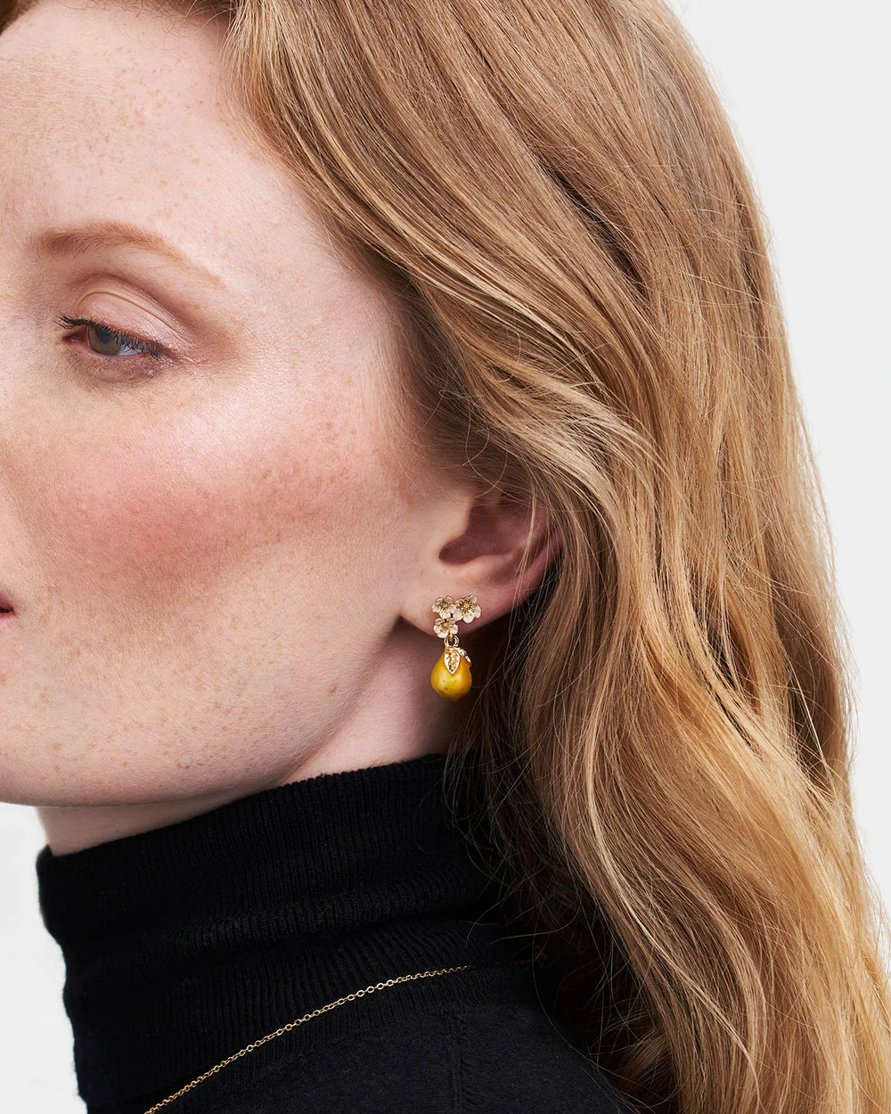 Gold drop earrings with floral design and yellow gemstone accent, worn by a woman in turtleneck.