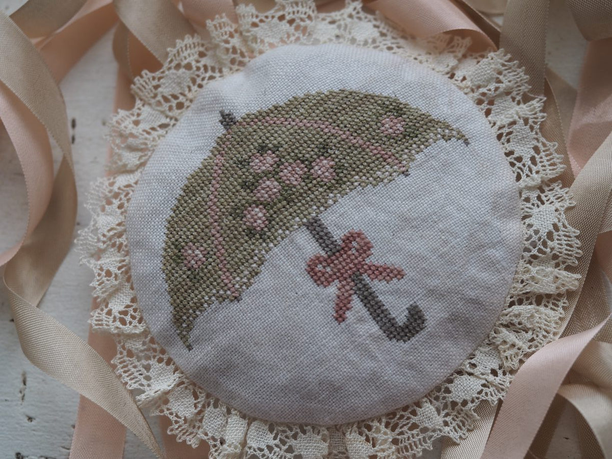 Handcrafted embroidery brooch featuring a green umbrella and pink flowers, with lace trim and satin ribbons.
