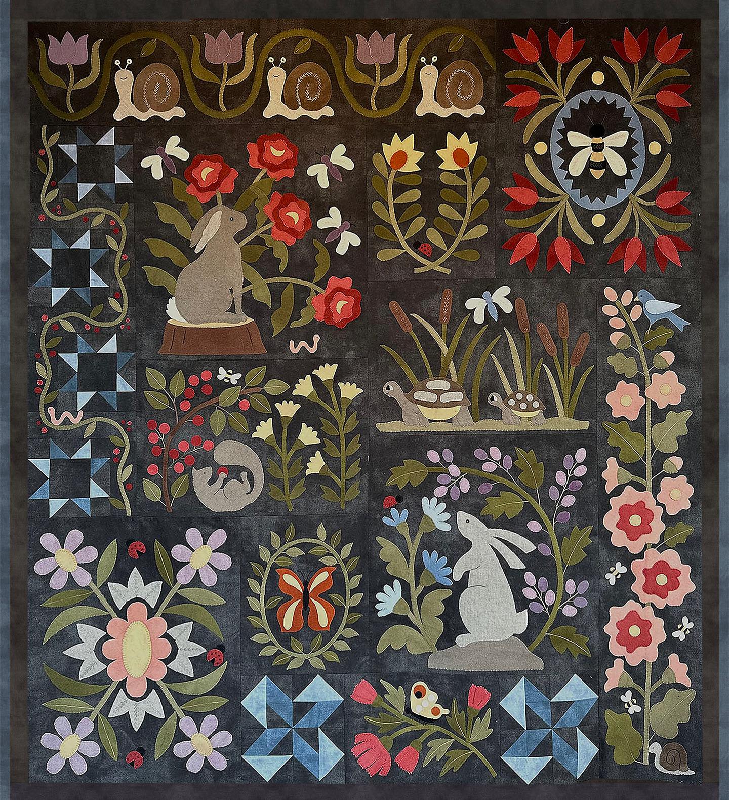 Colorful folk art quilt featuring rabbits, flowers, and snails on dark fabric; perfect for home decor.
