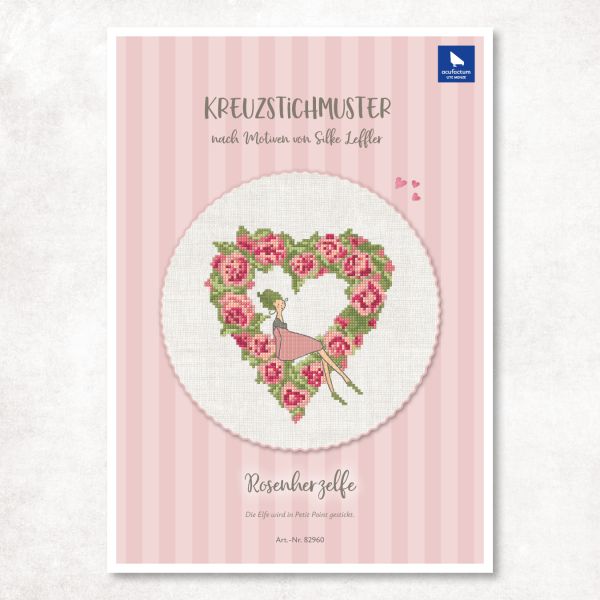Cross-stitch pattern featuring a heart of roses and a seated fairy in shades of pink and green.