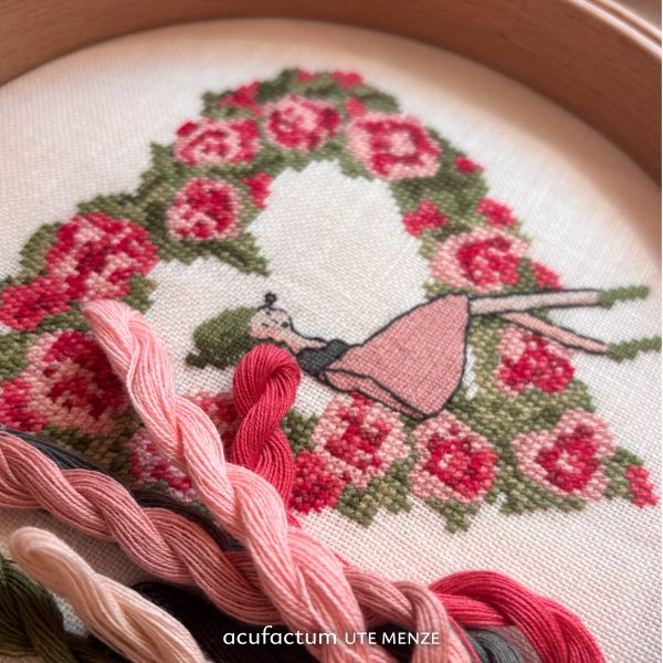 Embroidery kit featuring a rose wreath design, girl in a pink dress, includes colorful threads.