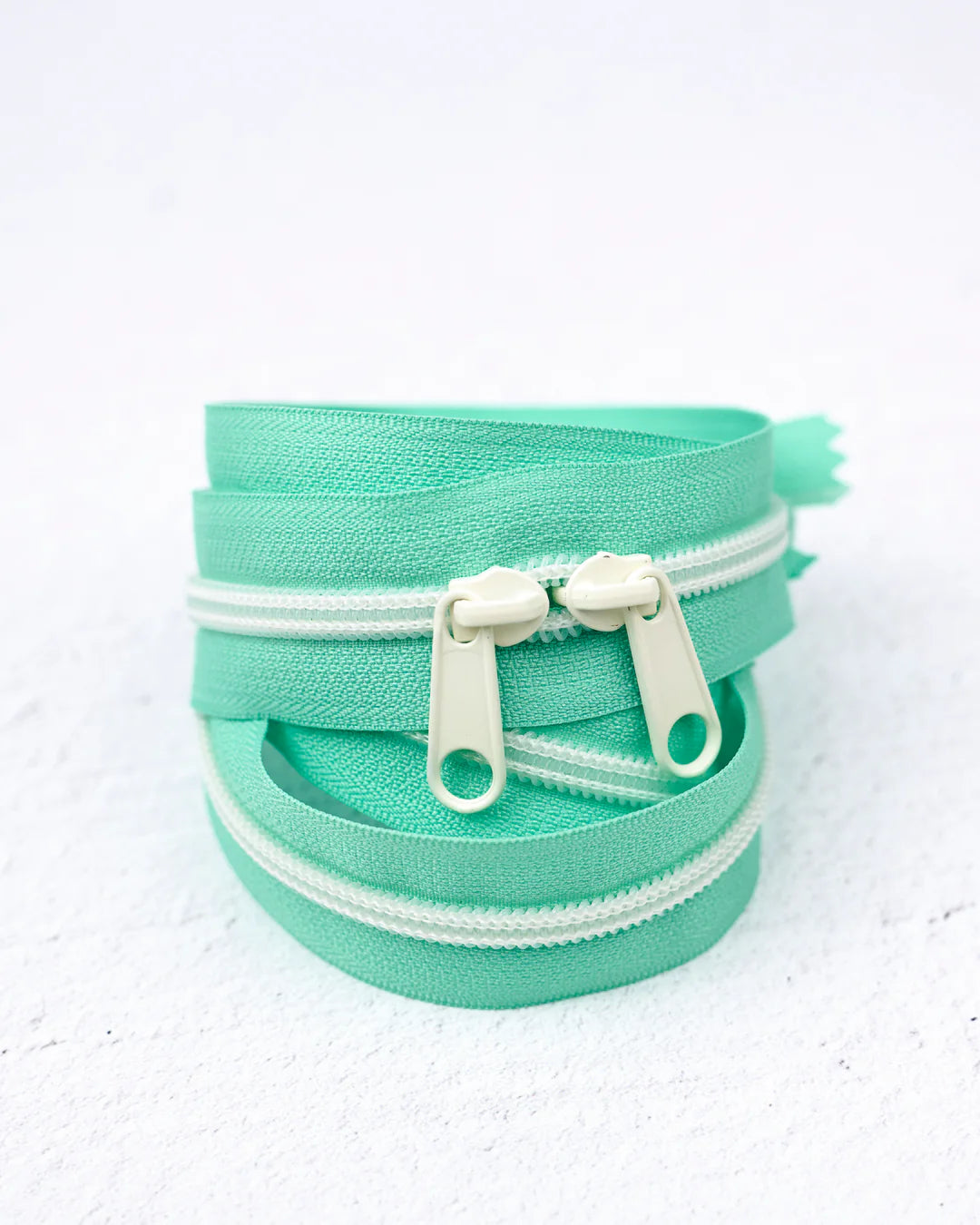 Mint green zippers with cream pulls, ideal for sewing and crafting projects.