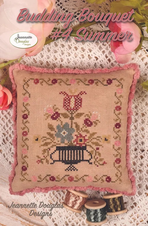 Budding Bouquet #4 Summer cross-stitch design, floral pattern on beige fabric with pink trim and spools of thread.