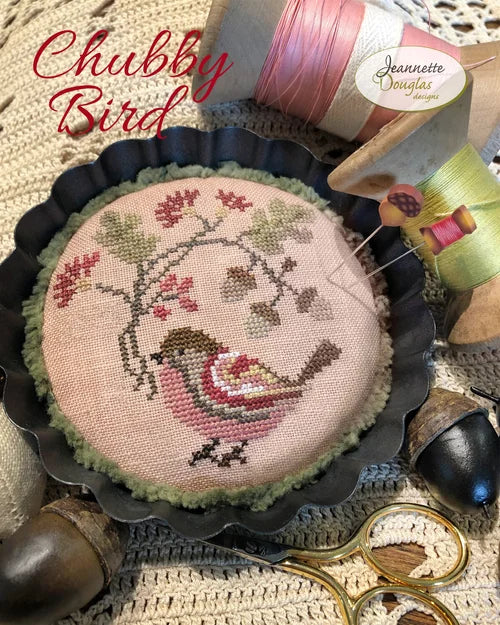 Chubby Bird needlework design in soft colors, featuring floral accents on a round fabric piece.