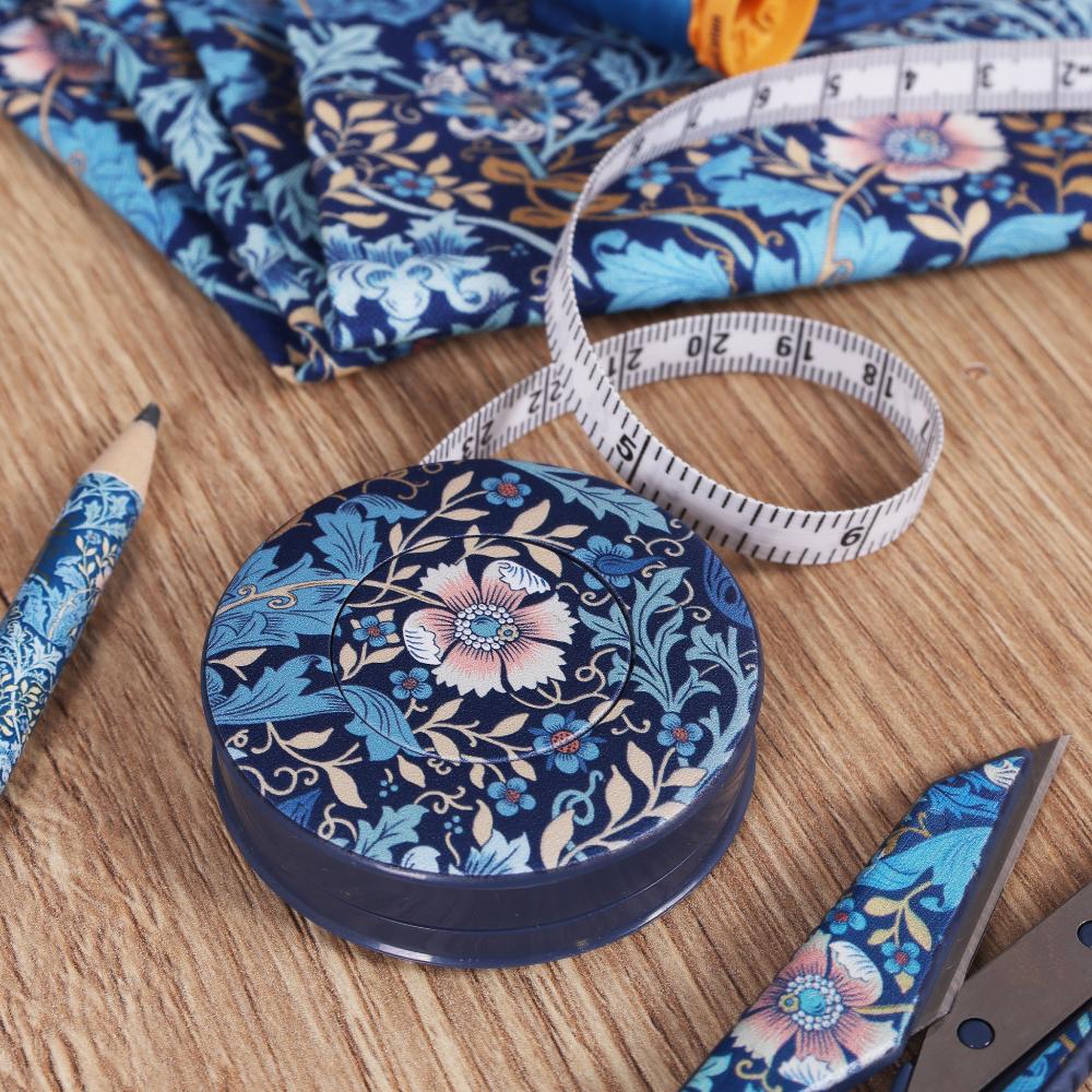 Navy floral fabric tape measure with blue fabric, pencil, and sewing tools on a wooden surface.