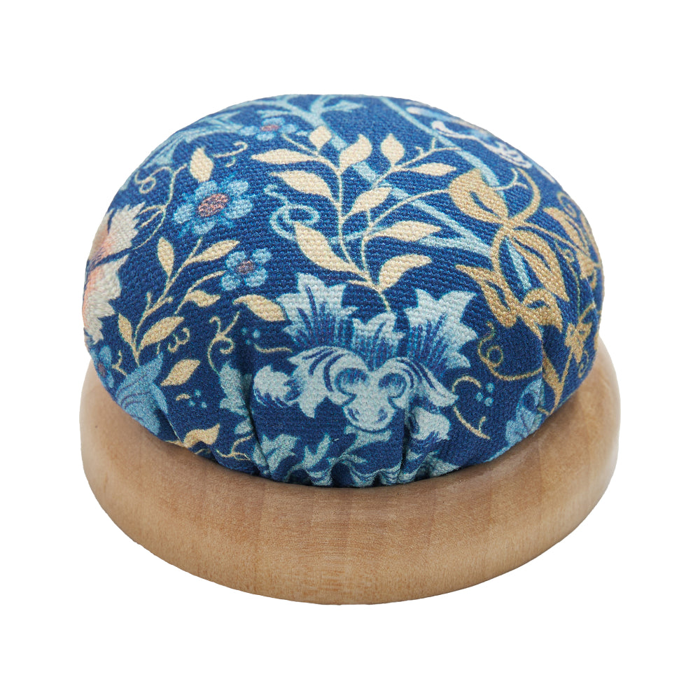Blue floral fabric pincushion with wooden base, ideal for sewing and crafting enthusiasts.