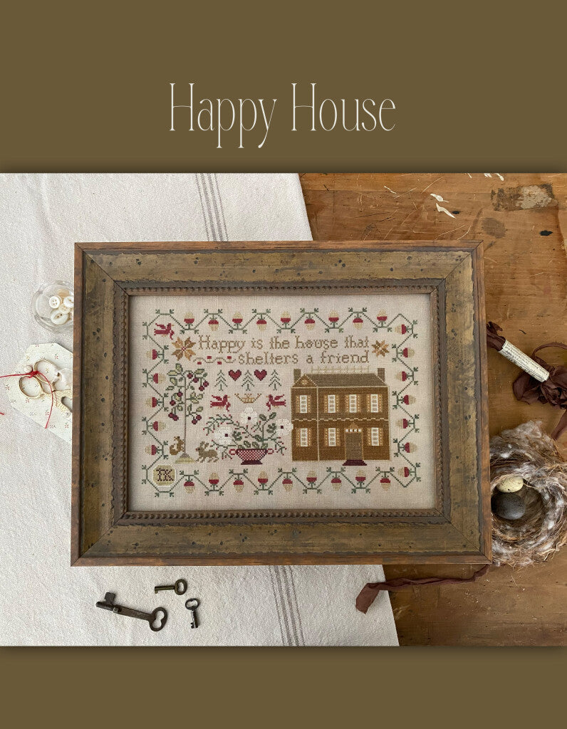 Framed cross-stitch art with a house, flowers, and text, vintage style, warm colors, home decor.