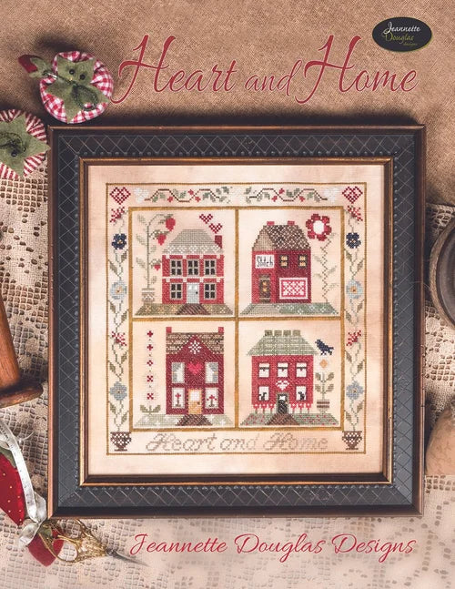Framed cross-stitch pattern featuring colorful houses, titled 'Heart and Home', by Jeannette Douglas Designs.