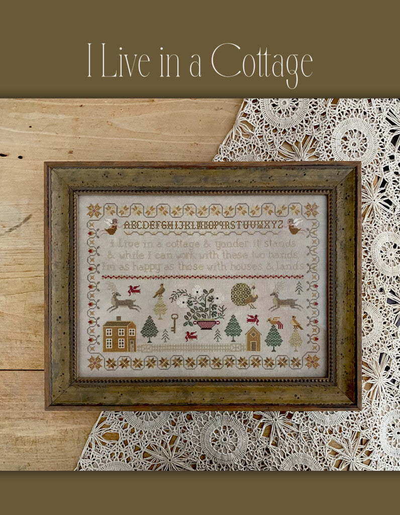 Framed cross-stitch art with whimsical cottage theme, featuring intricate designs and earthy colors.