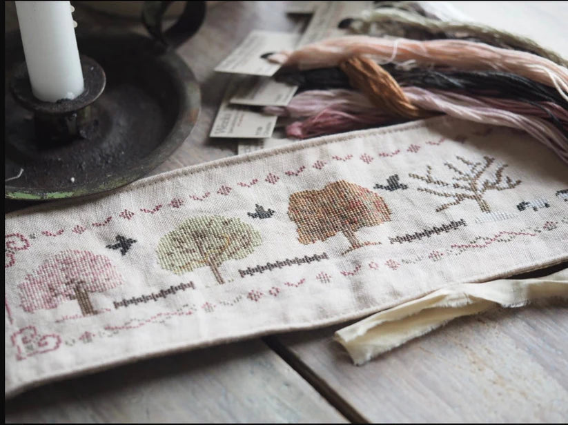 Embroidered linen fabric featuring colorful trees and birds, ideal for crafting and home decor.