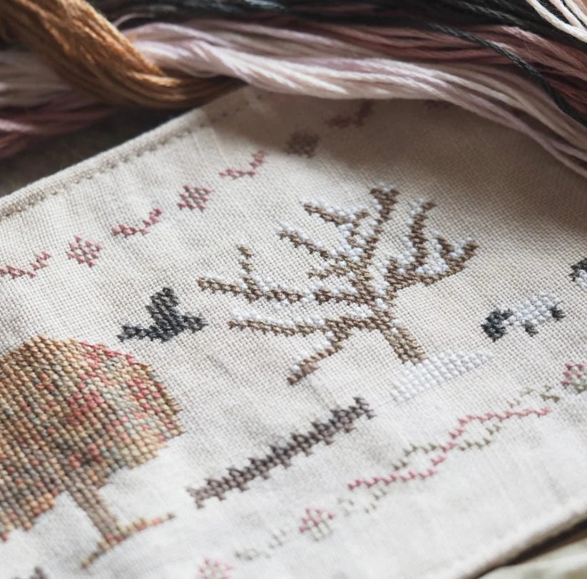 Intricate cross-stitch embroidery featuring a tree, birds, and sheep on light fabric. Ideal for crafting.