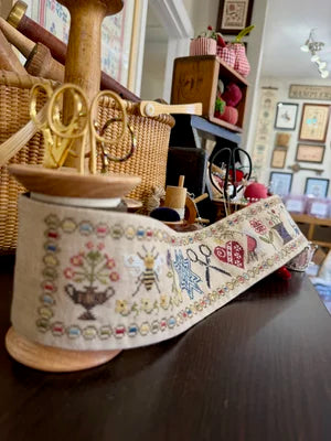Decorative sewing ribbon featuring floral and scissor patterns, made of fabric with a wooden spool.