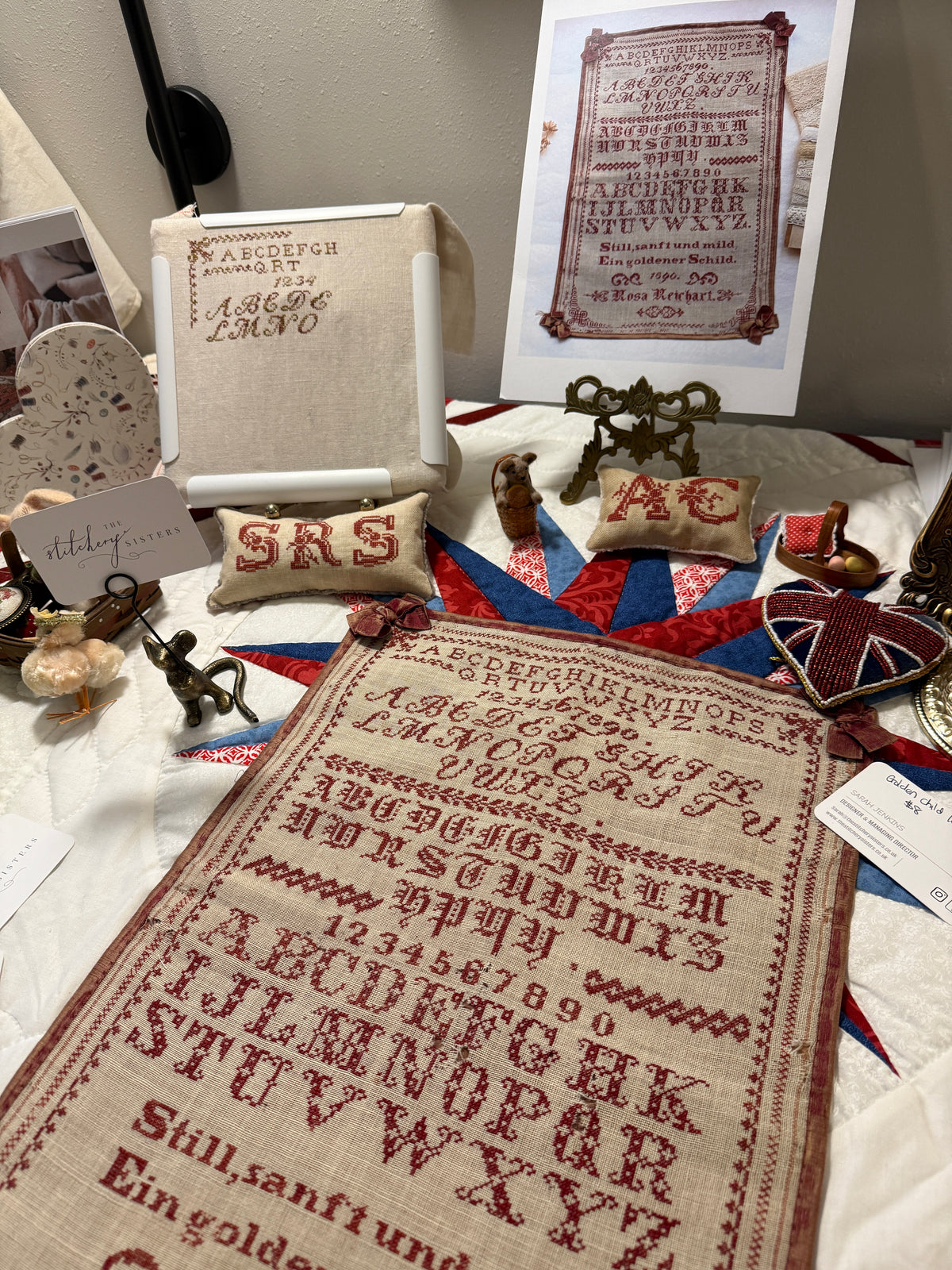Vintage handcrafted embroidery sampler in red on linen, featuring alphabet and numbers, decorative elements.
