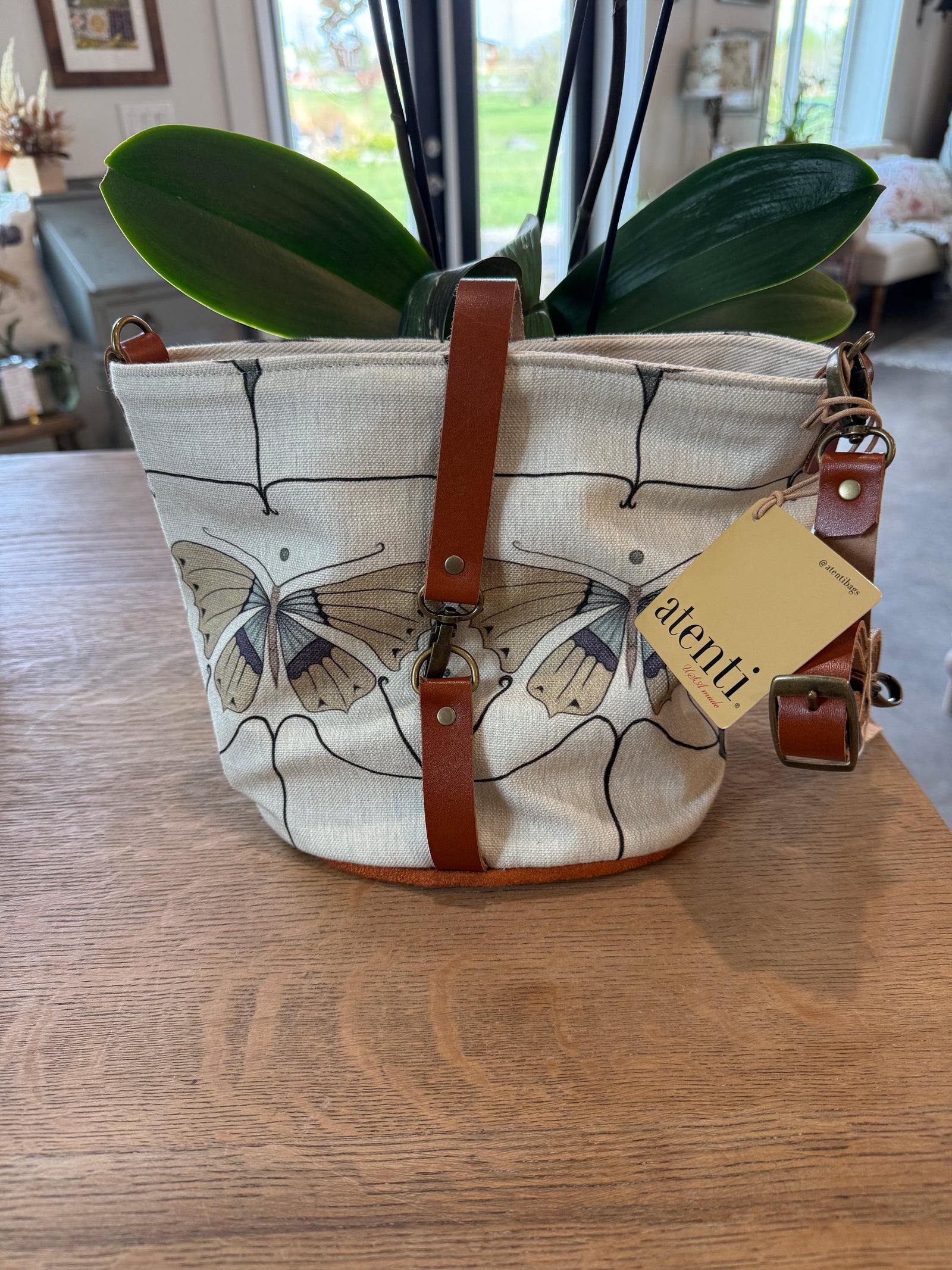 Canvas bucket bag with leather straps, featuring a butterfly print design and a warm neutral color.