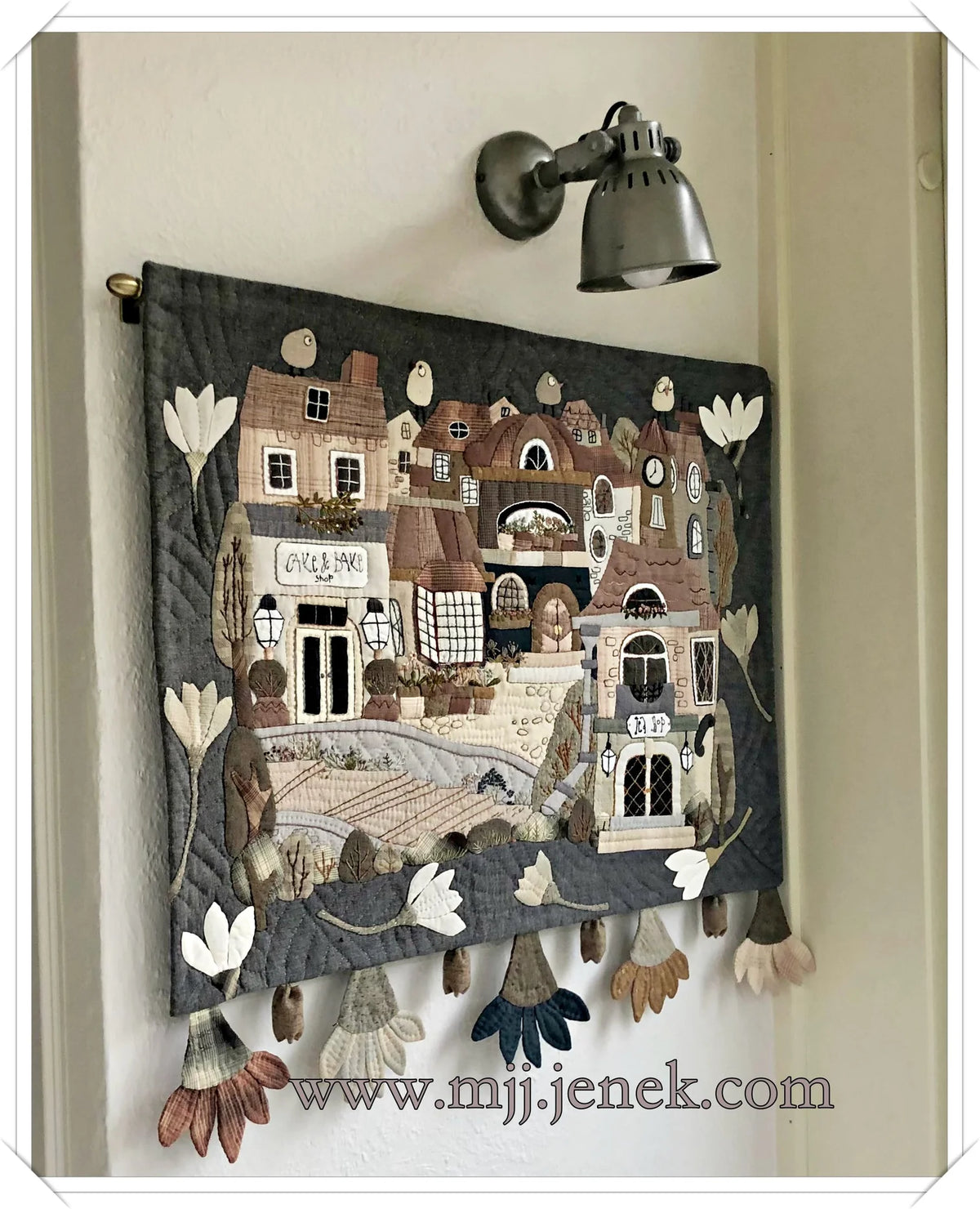 Handmade wall hanging quilt in gray with village scene, featuring decorative flowers and detailed stitching.