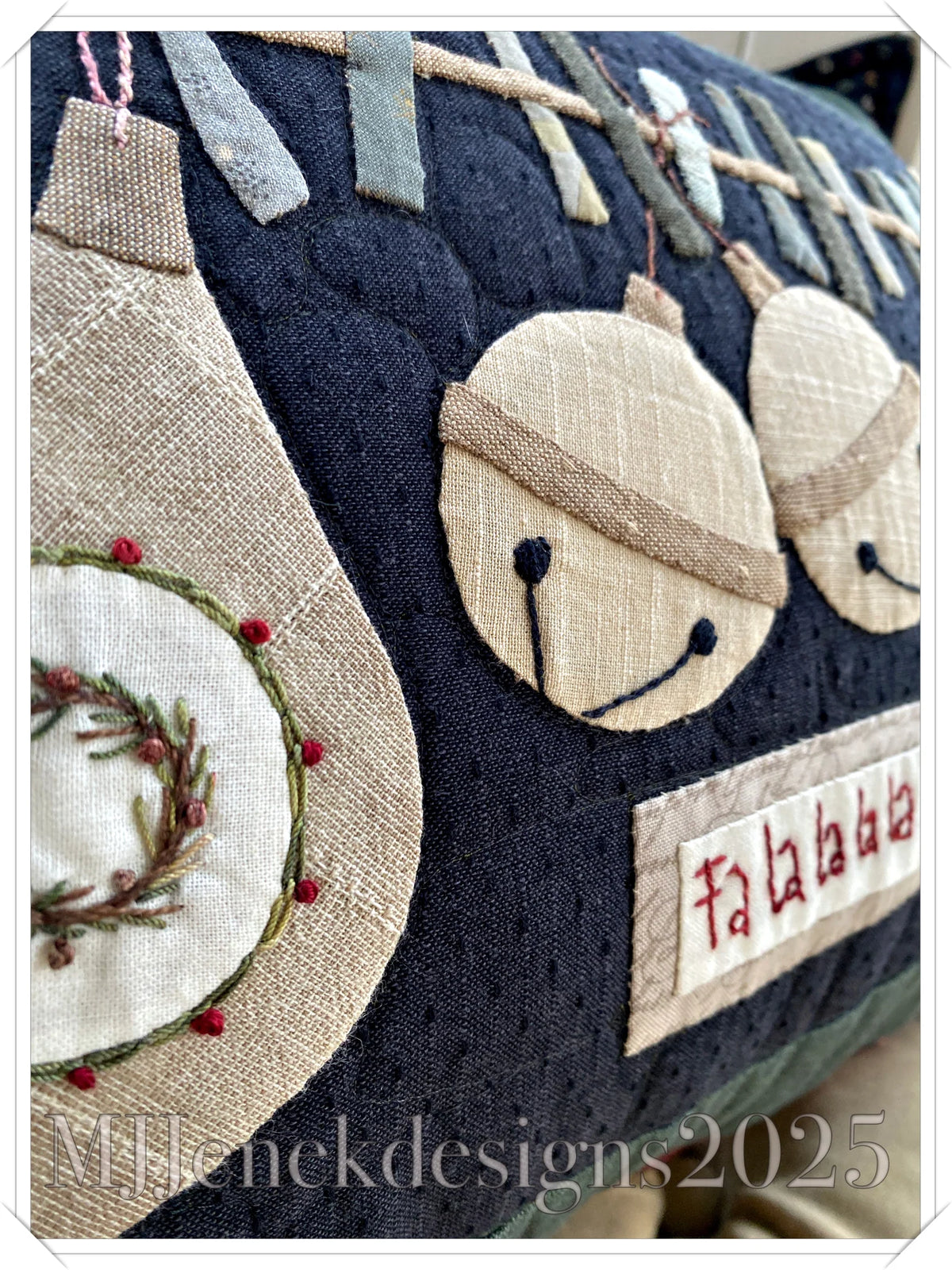 Handmade decorative pillow featuring embroidered bells and festive designs on navy fabric.