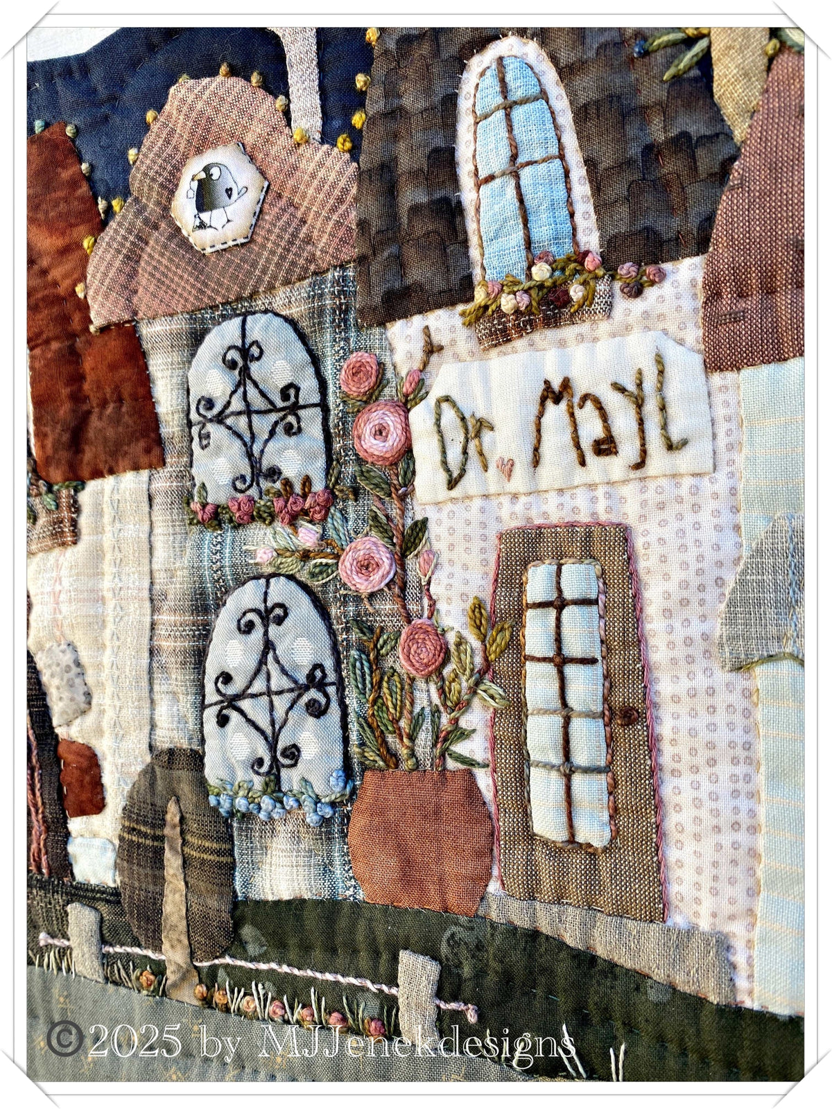 Artisan fabric wall hanging featuring whimsical houses, floral details, and intricate stitching, warm colors.