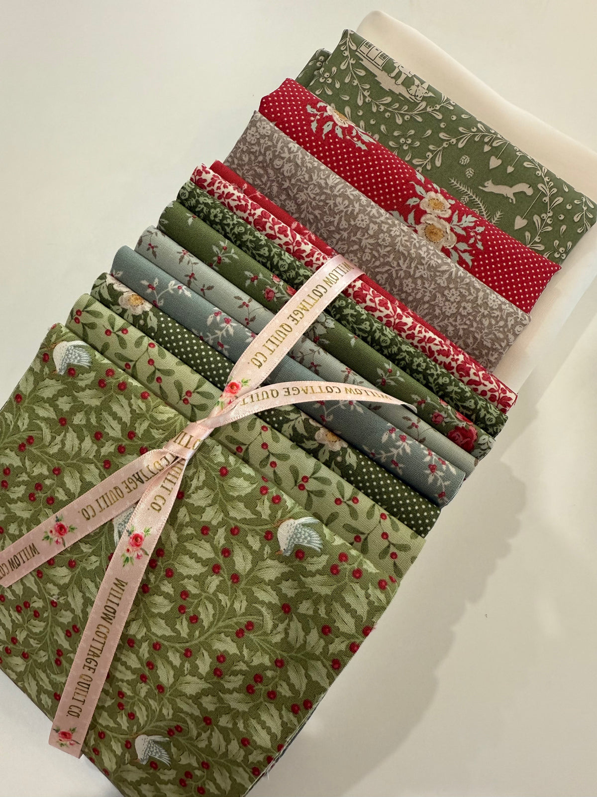 Set of twelve quilting cotton fabrics in red and green patterns, tied with a pink ribbon.