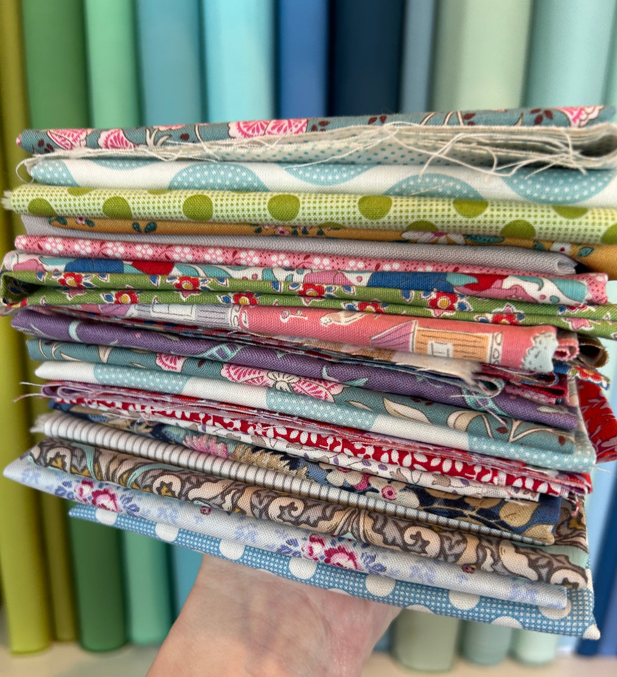 Stack of colorful cotton quilting fabrics featuring floral and polka dot patterns.