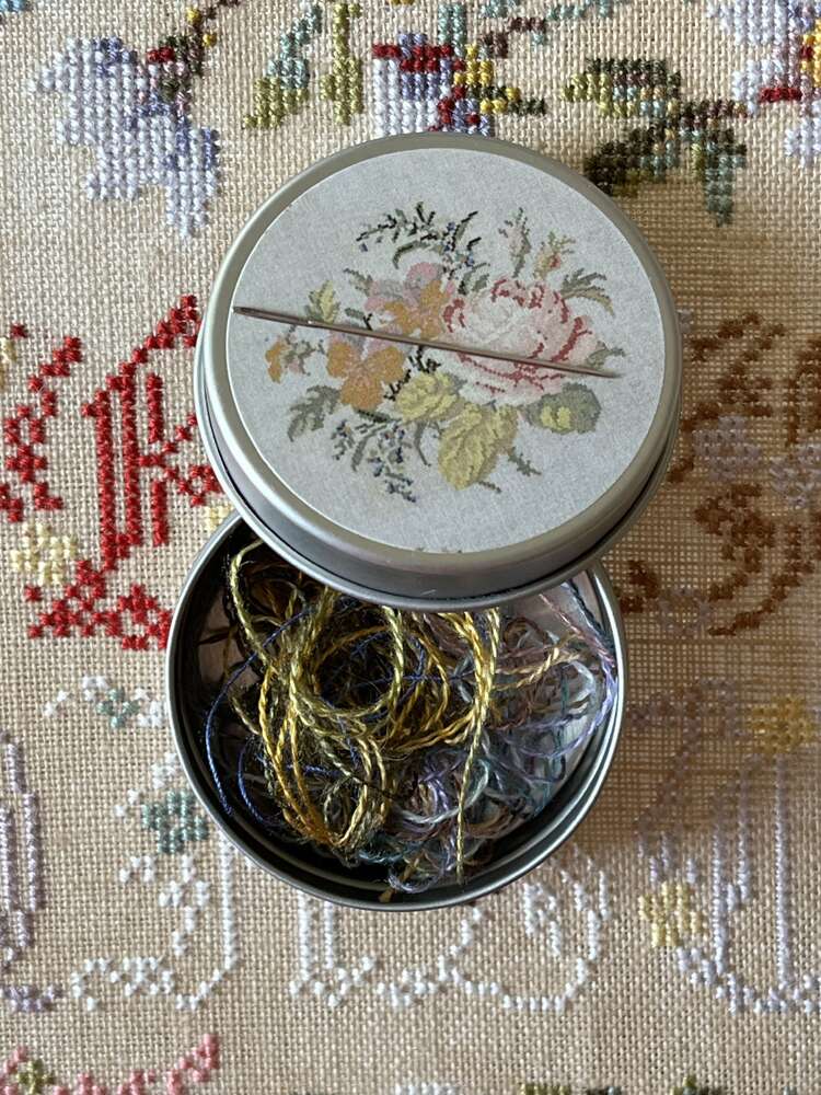 Vintage tin with floral design, containing colorful embroidery threads. Perfect for crafting and sewing projects.