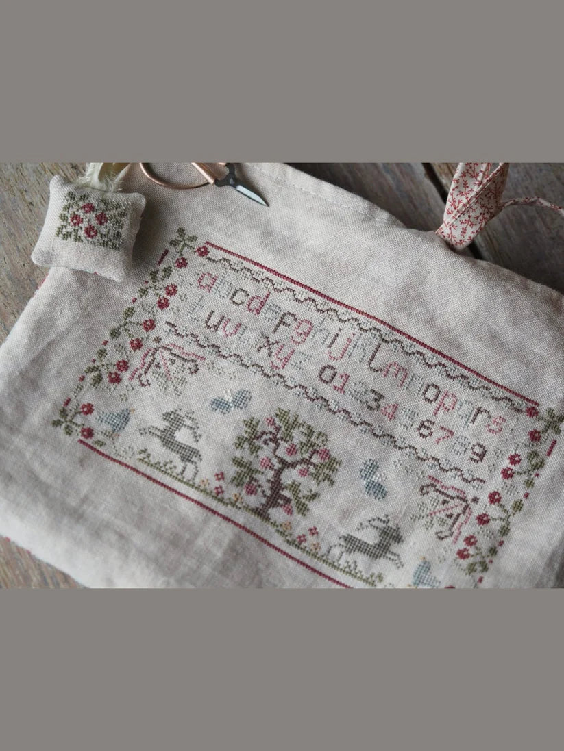 Embroidered linen fabric with alphabet and floral designs, featuring soft muted colors and a stitched pillow.
