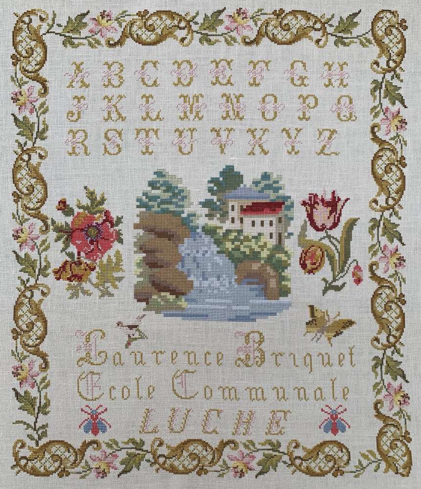 Vintage embroidery sampler with alphabet, floral designs, and a scenic river scene, in neutral colors.