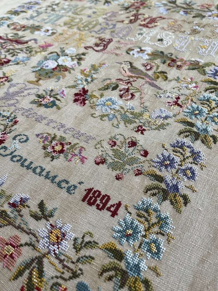 Vintage needlework fabric with floral patterns in pastel colors, dated 1894.