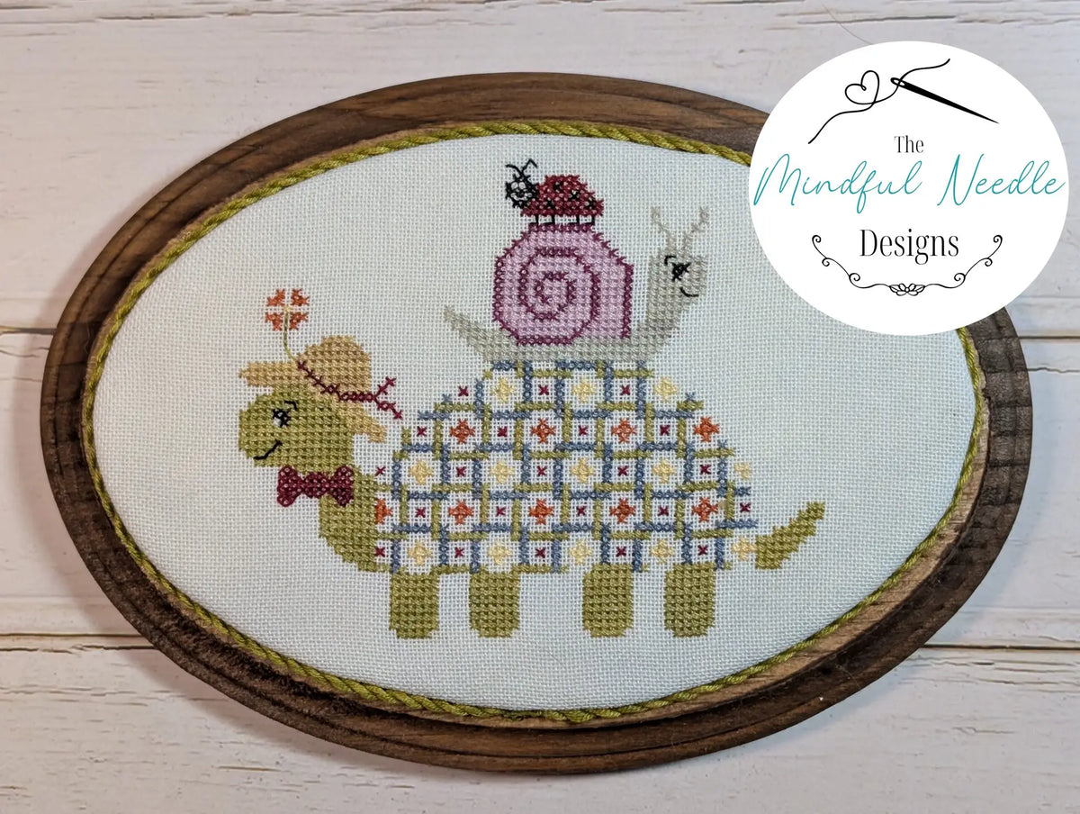 Cute cross-stitch art featuring a green turtle with a pink snail, framed in wooden embroidery hoop.