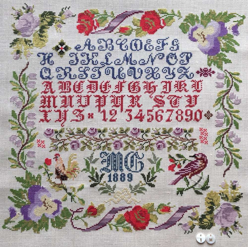 Antique embroidered sampler with alphabet, flowers, and birds, featuring colorful threads and intricate design.