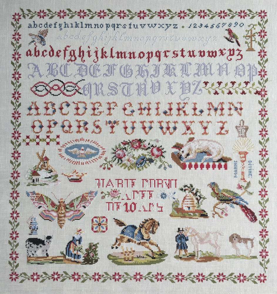 Vintage cross-stitch sampler featuring alphabets, animals, flowers, and decorative motifs on linen fabric.