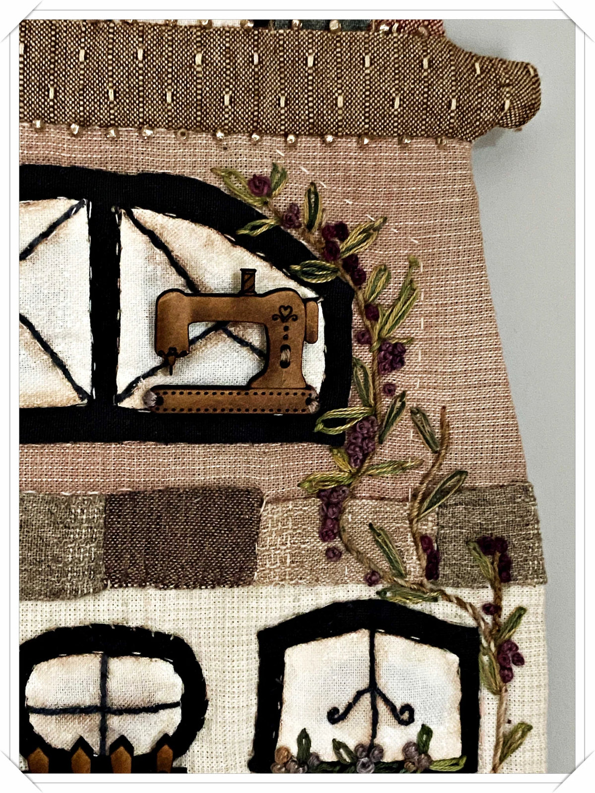 Decorative fabric wall art featuring a vintage sewing machine and floral embroidery, in warm beige tones.