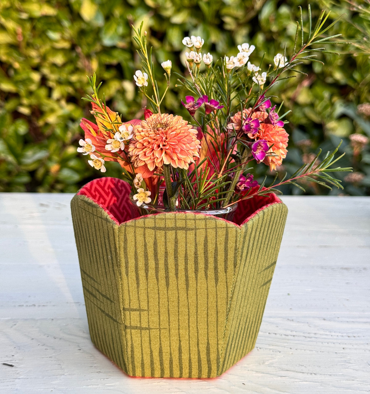 Green fabric flower vase with pink interior, filled with colorful flowers, perfect for home decor.