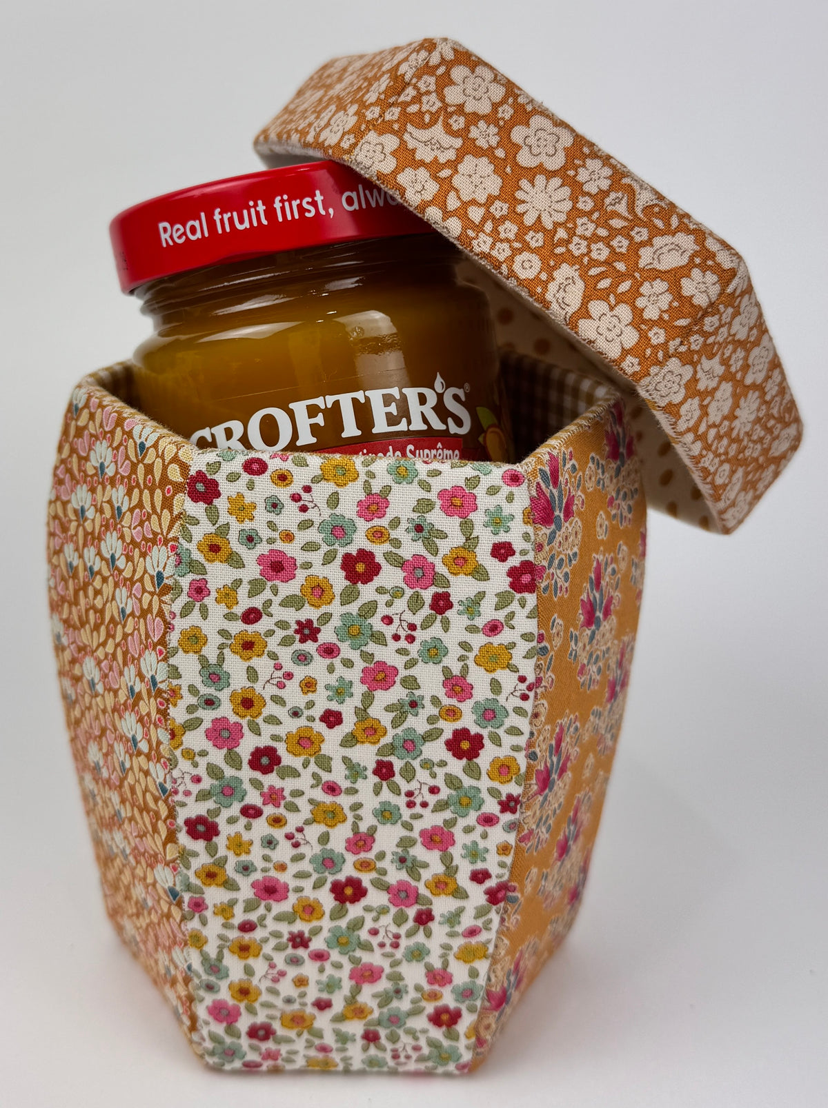 Colorful floral fabric container holding Crofter's fruit jam, featuring an orange floral lid.