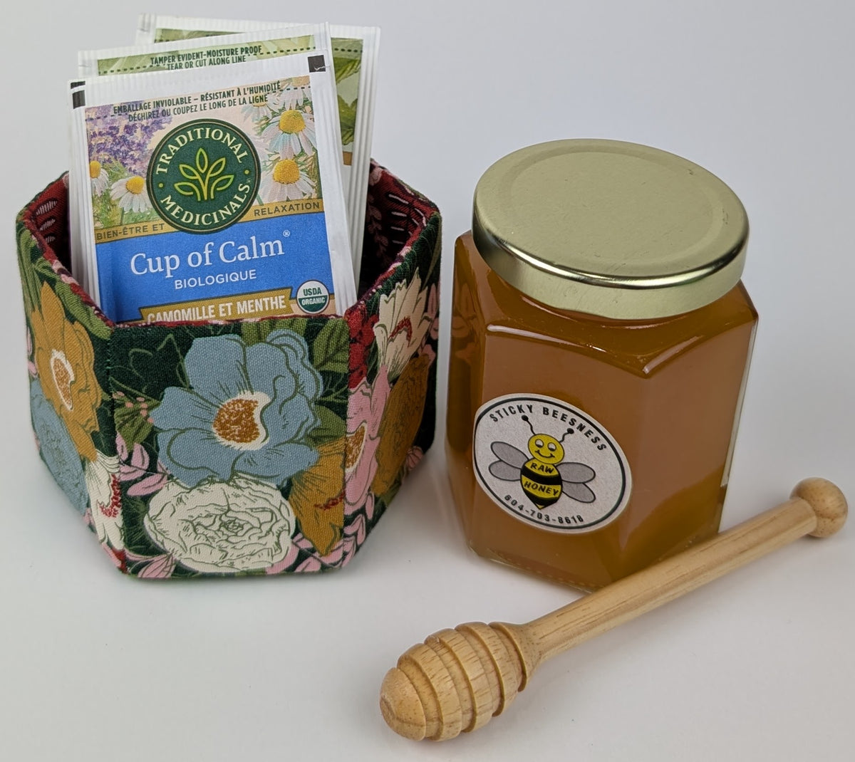 A floral fabric basket with herbal tea bags, raw honey jar, and honey dipper, perfect for relaxation.
