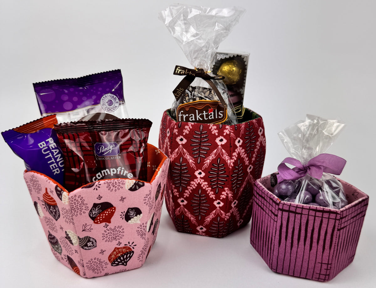Set of three colorful fabric baskets: pink floral, red patterned, and purple striped, holding assorted snacks.