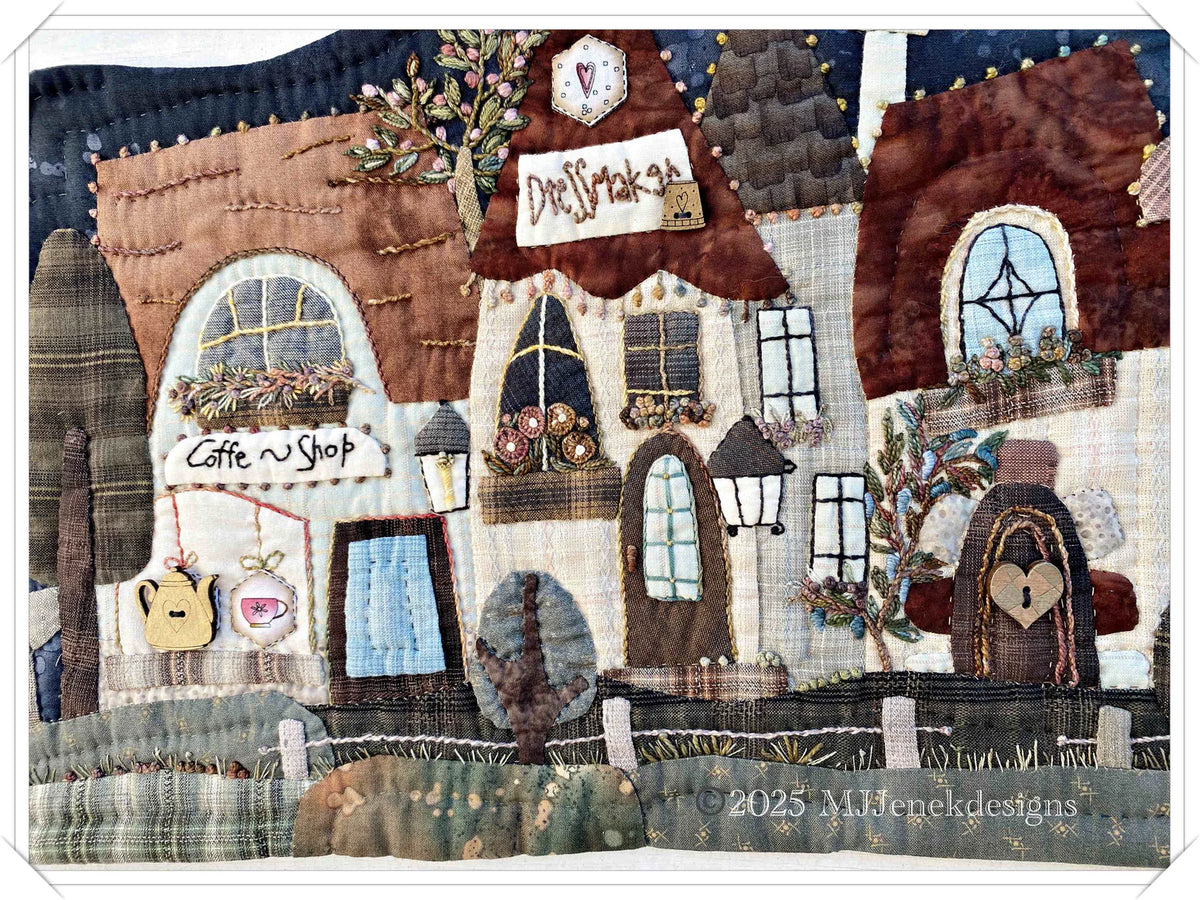 Quilted fabric art depicting a charming coffee shop with brown roofs and decorative windows.