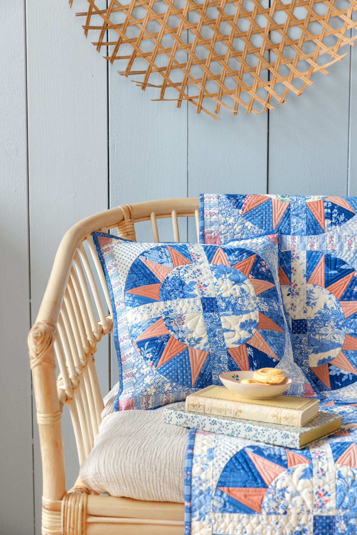 Blue and peach quilted throw pillow and blanket in floral patterns on a rustic rattan chair.