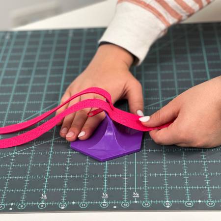 Hand using a purple crafting tool with pink straps on a cutting mat for easy material handling.