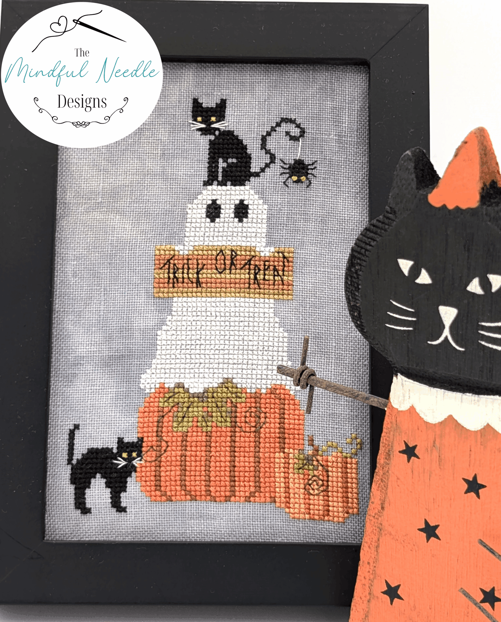 Halloween cross-stitch art featuring cats and pumpkins, framed in black, fun fall decor.